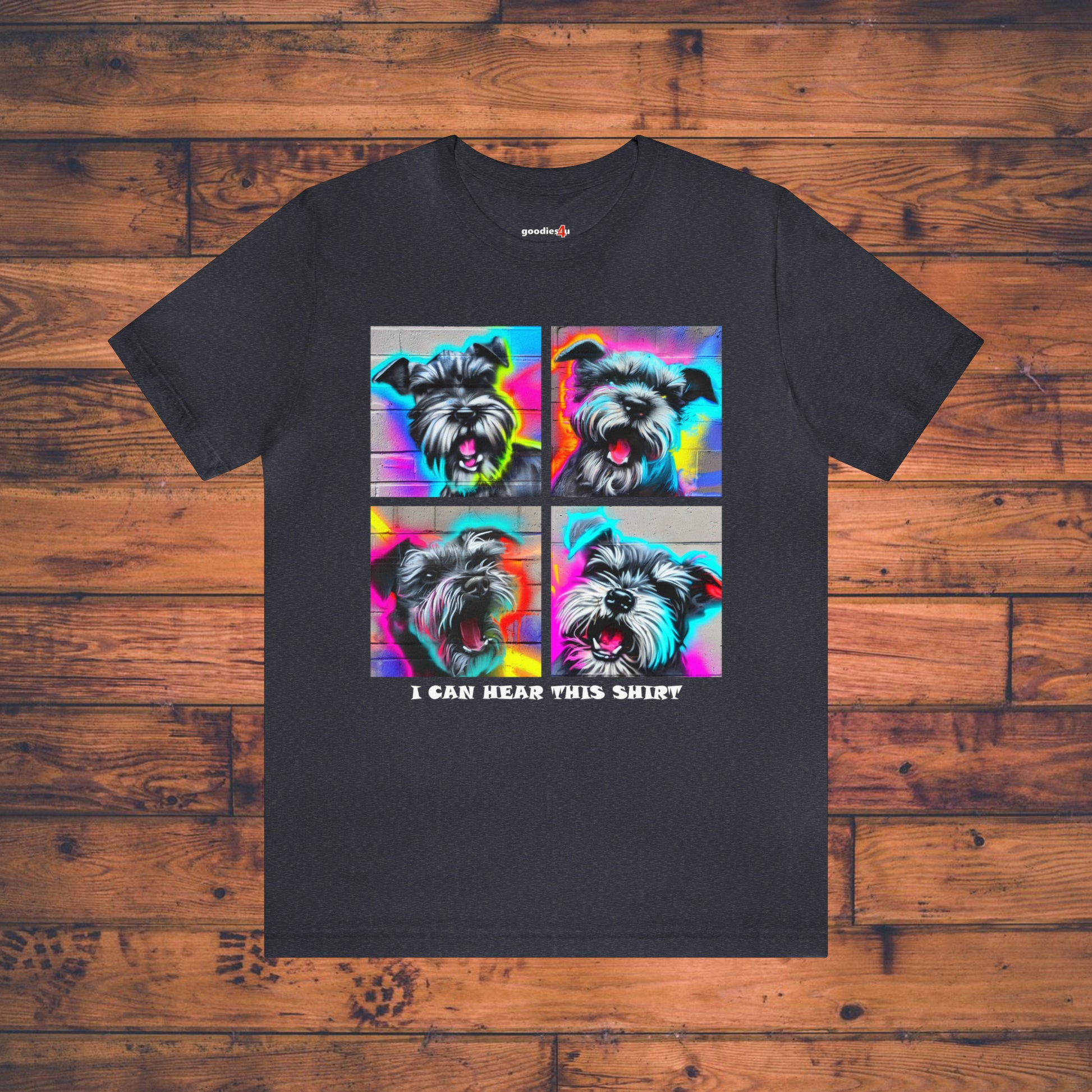 A dark navy t shirt that has four graffiti-style images of barking miniature schnauzers and the text "I Can Hear This Shirt" on a wood floor.