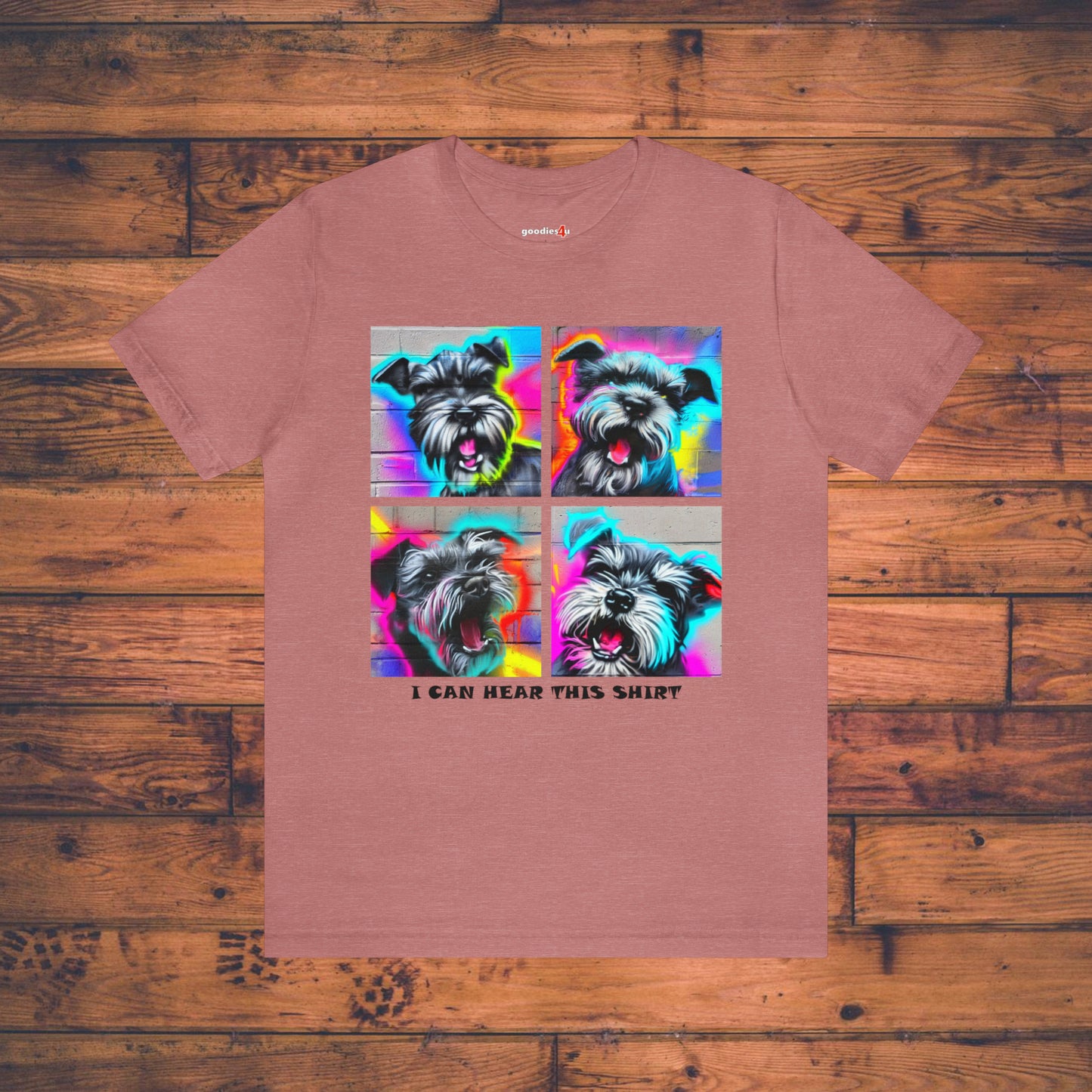 A heather mauve t shirt that has four graffiti-style images of barking miniature schnauzers and the text "I Can Hear This Shirt" on a wood floor.