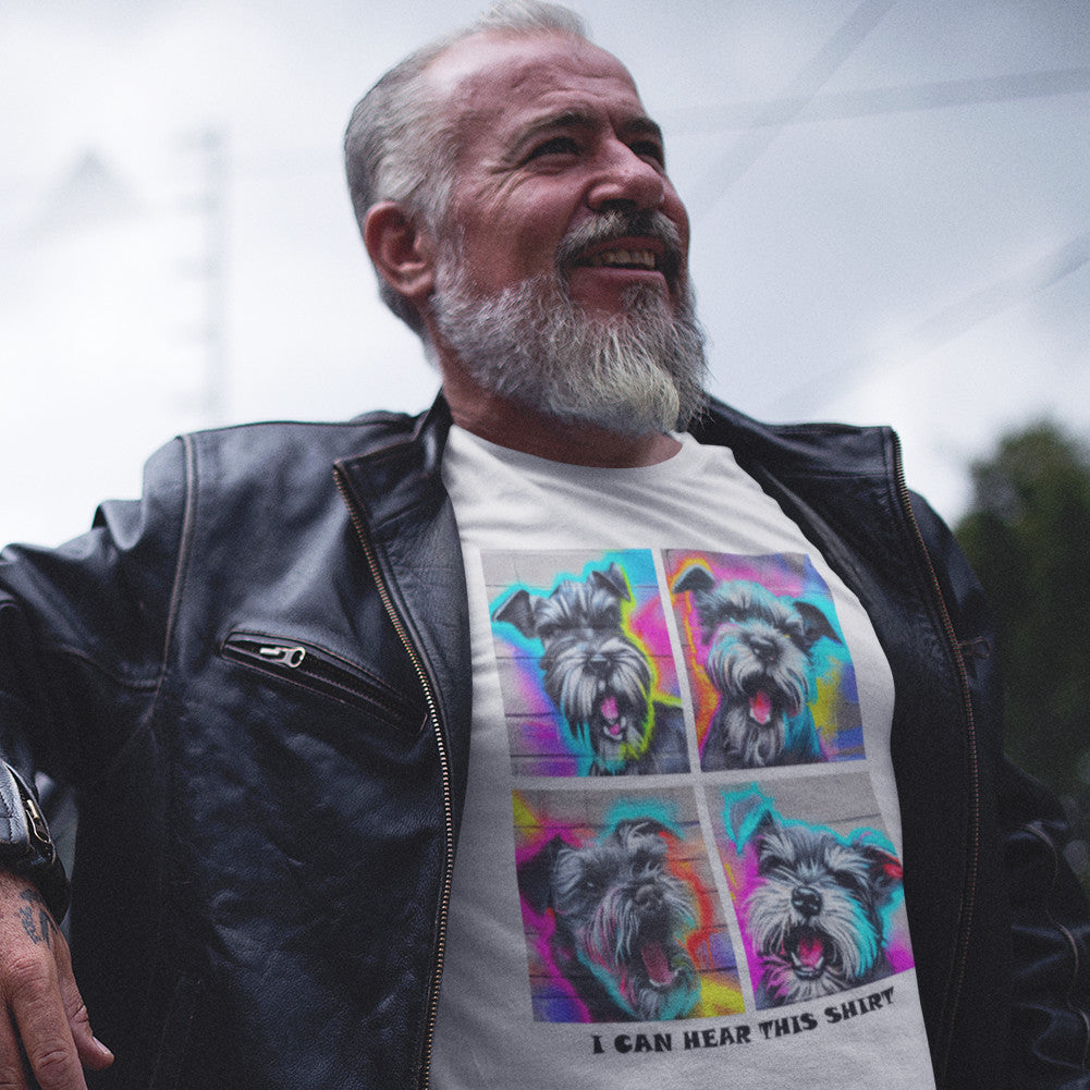 A smiling man wearing a white t shirt that has four graffiti-style images of barking miniature schnauzers and the text "I Can Hear This Shirt"